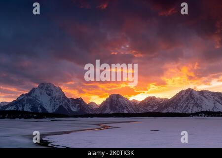 Ein feuriger Sonnenuntergang, der den Himmel über einem auftauenden Jackson Lake aus der Wintersaison erhellt. Grand Teton National Park, Wyoming Stockfoto