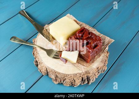 Goldene Gabel mit Stücken Guava-Süße und Käse auf einem Holzteller, neben einem Messer. Stockfoto