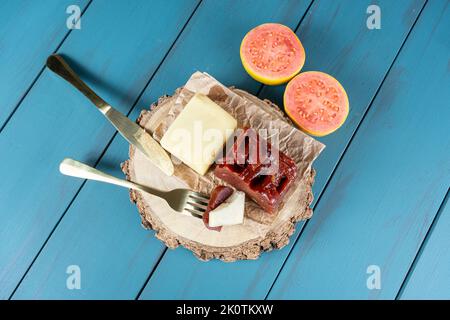 Goldene Gabel mit Stücken von Guava süß mit Käse auf einem Holzteller, neben einem Messer und einem Guava. Stockfoto