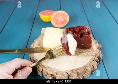 Mann, der eine Gabel mit Guava-Süssstücken mit Käse auf einem Holzbrett hält. Stockfoto