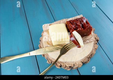 Goldene Gabel mit Guava-Süß- und Käsestücken auf einem Holzteller, neben einer Messeransicht. Stockfoto