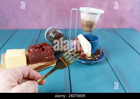 Mann, der eine Gabel mit Guava-Stücken mit Käse hält. Im unscharfen Hintergrund Bohnen und Kaffeetasse. Stockfoto