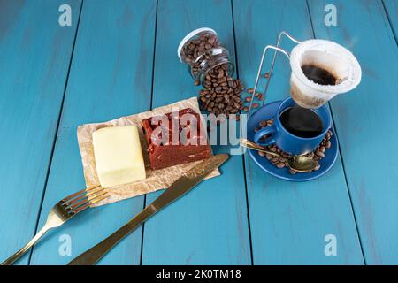 Guava süß mit Käse auf braunem Papier, umgeben von Besteck, Bohnen und einer Tasse Kaffee. Stockfoto