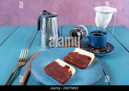 Guava süß mit Käse, umgeben von Besteck, Tasse und Kaffeebohnen auf einem blauen Tisch. Stockfoto