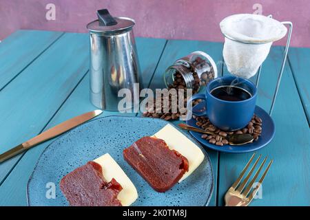 Nahaufnahme von Guava süß mit Käse, umgeben von Besteck, Tasse und Kaffeebohnen, auf einem blauen Tisch. Stockfoto