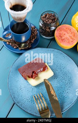 Guava-Süße und Käse in Scheiben neben Besteck und Bohnen und einer Tasse Kaffee. Stockfoto