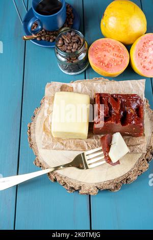 Gabel mit Stücken von Guava süß mit Käse auf einem Holzbrett, neben Bohnen und Tasse Kaffee vertikal. Stockfoto