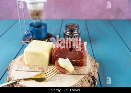 Gabel mit Stücken von Guava süß mit Käse auf einem Holzbrett, neben Bohnen und Tasse Kaffee. Stockfoto