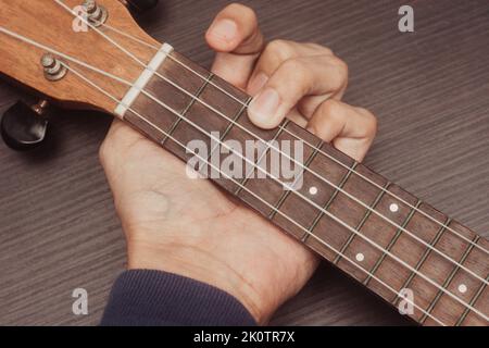 Ukulele in Nahaufnahme mit handplatzierten Akkorden. Der Akkord ist C. Tragbares Saiteninstrument. Konzept zur Musikerstellung. Isolierter Holzhintergrund. Stockfoto