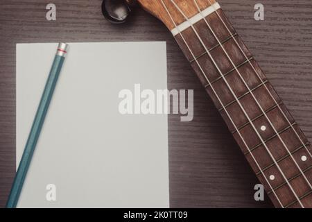 Ukulele in Nahaufnahme mit einem Blatt Papier, um Noten aufzuschreiben. Konzept der musikalischen Komposition und Kreation. Isolierter Holzhintergrund. Stockfoto