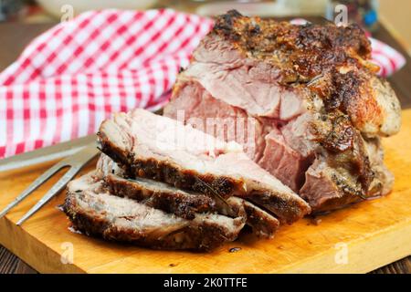 Gebackenes Schweinefleisch mit Gewürzen auf braunem Schneidebrett mit Messer und Gabel geschnitten. Stockfoto