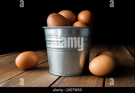 Frische Eier in einem kleinen Blecheimer, Eimer oder Metallbehälter. Komposition auf Holztisch. Stockfoto