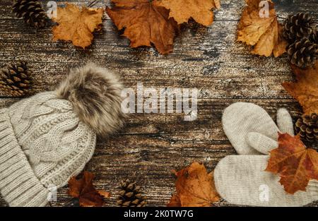 Warme, kuschelige Wintermütze mit Bommel und Handschuhen. Herbst flach Lay Zusammensetzung, mit Kegeln und Herbst Herbstblätter auf Holzgrund. Stockfoto