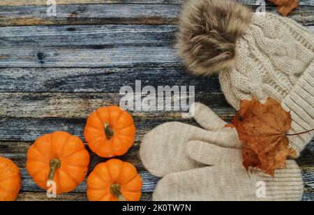 Warme, kuschelige Wintermütze mit Bommel und Handschuhen. Herbst flach Lay Komposition mit Kürbissen, Herbstblättern und Kopierraum auf Holzhintergrund. Stockfoto