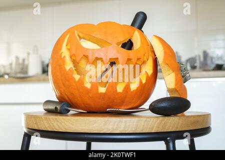 Geschnitzter Halloween-Kürbis, Jack Lantern und Schnitzwerkzeuge. Das gruselige Jack-o'-Laternen-Gesicht wurde mit Löffelrinne und Sägeblättern zerschnitten. Stockfoto