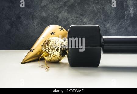 Kurzhantel, goldene Dekoration und Partyhut für Silvesterfeier. Gesundes Fitness-Lifestyle-Konzept. Fitness-Workout alles gute zum neuen Jahr. Stockfoto