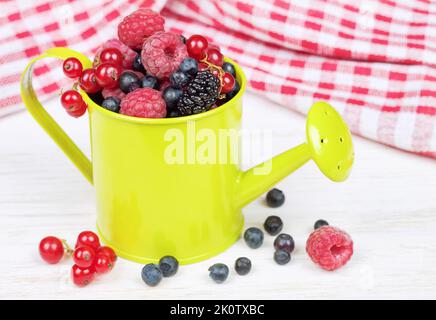 Mischung der Beeren in einer kleinen hellgrünen dekorativen Gießkanne auf weißem Holzgrund. Erdbeere, Himbeere, Maulbeere, rote Johannisbeere, Heidelbeere Stockfoto