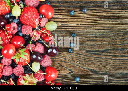 Mischung aus frischen Beeren auf braunem Holzgrund. Erdbeeren, Kirschen, Himbeeren, Stachelbeeren, rote Johannisbeeren, Blaubeeren. Draufsicht, flaches Lagenmodell Stockfoto