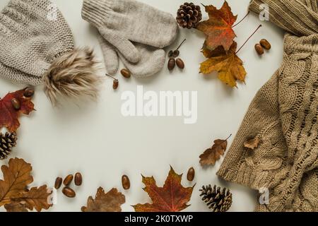 Warmer, kuscheliger Winterpullover, Handschuhe und Mütze mit Bommel. Herbst flach Lay Zusammensetzung mit Eicheln, Zapfen, Herbstblätter und weißen Kopieplatz. Stockfoto