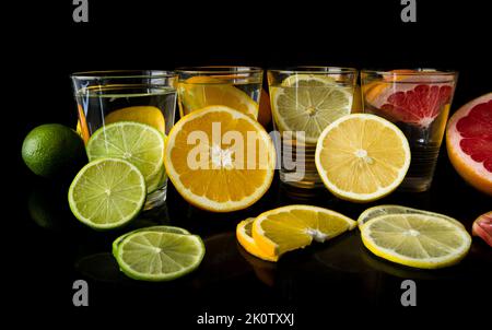 Vier Gläser Wasser mit Limetten, Orange, Zitrone und Grapefruit. Komposition wird auf schwarzem Hintergrund aktualisiert. Stockfoto