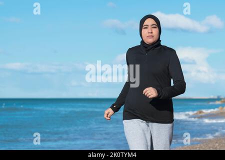 Arabische Frau, die am Strand in der Nähe des Meeres läuft Stockfoto