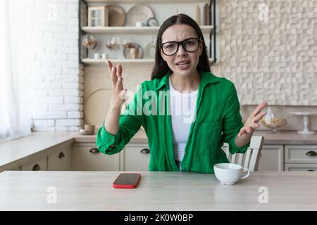 Online-Beratung mit einem Psychologen. Junge Frau in Brille bei einem Online-Termin mit einem Psychologen. Zu Hause sitzen und die Kamera betrachten. Nervös, unzufrieden, winkend ihre Hände Stockfoto