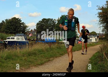 Ken-Läufer Nr. 26 macht vor Läufer Nr. 13, da sie an festfahrenden Booten vorbeifahren, während sie am langen Kanalrennen 2022 von Liverpool nach Leeds teilnehmen Stockfoto