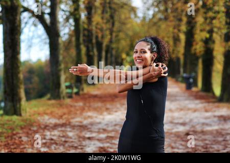 Positive Frau mittleren Alters Stretching im Freien Vorbereitung auf die Ausübung in Sportbekleidung Stockfoto