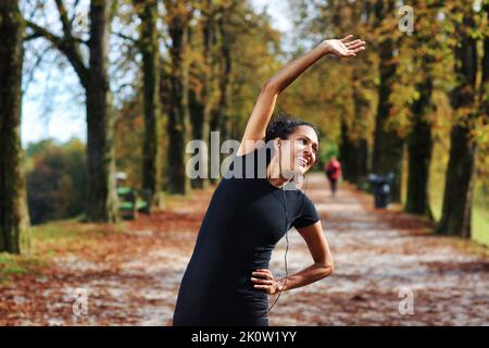 Positive Frau, die sich im Freien dehnt, bereitet sich auf Sport in Sportbekleidung vor Stockfoto