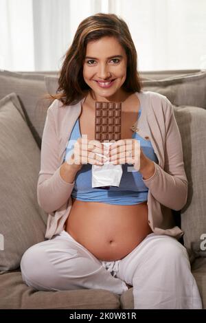 Wenn das Verlangen eingreift. Eine junge Schwangere, die zu Hause eine Schokoladenplatte isst. Stockfoto