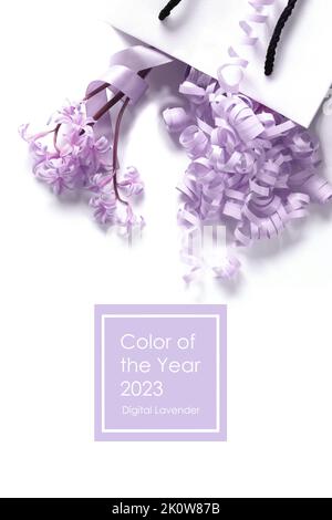 Weiße Geschenkbox mit frühlingshaften Fliederblüten und Lavendelserpentin auf weißem Hintergrund. Konzept der trendigen Lavendelfarbe. Text Farbe des Jahres 2023 Digitaler Lavendel Stockfoto
