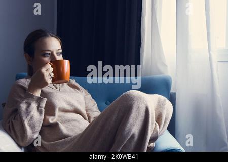 Junge Dame, die auf der Couch sitzt und Kaffee trinkt Stockfoto