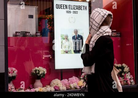 London, Großbritannien. 13.. September 2022. Frau geht an einem Schaufenster vorbei, auf dem das Foto der längsten regierenden Monarchin, Königin Elisabeth II. Und ihres Mannes, zu sehen ist, während der Sarg mit ihrem Körper am 13. September 2022 im Buckingham Palace in London, Großbritannien, eintreffen wird. Elisabeth II. Verstarb am 8. September in Schottland. Ihre Überreste nach den Zeremonien in Edinburgh werden am 13. September nach London verlegt und die Öffentlichkeit darf den Palast besuchen, um Respekt zu zollen. (Foto von Dominika Zarzycka/Sipa USA) Quelle: SIPA USA/Alamy Live News Stockfoto