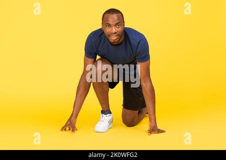 Afrikanischer Männlicher Läufer, Der In Der Crouch-Startposition Steht, Gelber Hintergrund Stockfoto