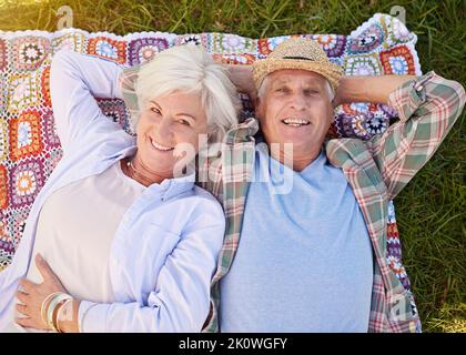 Es ist unsere Zeit zum Entspannen. Porträt eines glücklichen Seniorenpaares, das sich auf dem Rasen entspannt. Stockfoto