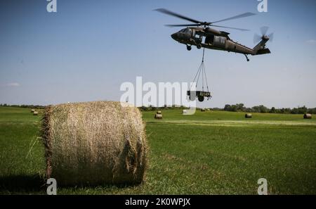 Ein Feld von Heuballen umrahmt eine Iowa Army National Guard UH-60 Black Hawk, während es einen Anhänger während eines U.S. Pathfinder Kurses im Camp Dodge in Johnston, Iowa, am 8. September 2022 belädt. Fast 30 Soldaten absolvierten den Kurs, der von einem mobilen Trainingsteam im Warrior Training Center der Army National Guard in Fort Benning, Georgia, unterrichtet wurde. Army Pathfinders werden geschult, um Navigationshilfe und Beratungsdienste für Militärflugzeuge in Gebieten zu leisten, die von unterstützten Einheiten-Kommandeuren bestimmt werden. Während des Pathfinder-Kurses werden die Studenten in der Flugzeugorientierung, der aerodynamischen Evakuierung, c Stockfoto