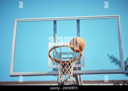 Basketballplatz, Sport und Reifen oder Ringnetz gegen einen blauen Himmel draußen. Sport-, Wettbewerbs- und Spaßhobby für Sportler mit einem Ball auf dem Korb Stockfoto