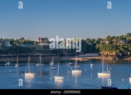 St. Malo, Bretagne, Frankreich - 8. Juli 2022: Morgenlicht auf weißen Yachten an der blauen Rance-Flussmündung mit ikonischen Gebäuden am grünen Ufer der Pointe de l Stockfoto