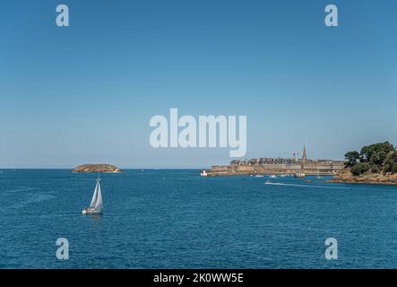 St. Malo, Bretagne, Frankreich - 8. Juli 2022: Die historische Altstadt mit ihren hohen Palästen hinter den Stadtmauern ragt unter blauem Himmel in den Ärmelkanal Stockfoto