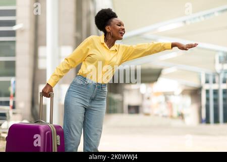 Glückliche afroamerikanische Frau Hailing Ein Taxi in der Nähe des Flughafens Stockfoto