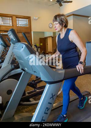 Ältere oder ältere Frau mittleren Alters, die ein Laufband in einem Fitnessstudio benutzt oder darauf läuft oder es benutzt. Stockfoto