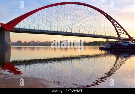 Eine große Bogenbrücke im Morgengrauen. Bugrinsky Brücke über den ob Fluss am Rande einer Großstadt. Nowosibirsk, Sibirien, Russland, 2022 Stockfoto