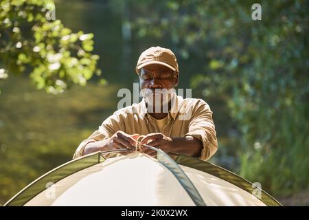 Serious Senior African American Backpacker tippen Knoten auf dem Zelt, während es in den Wald während der Wanderung am Wochenende Stockfoto