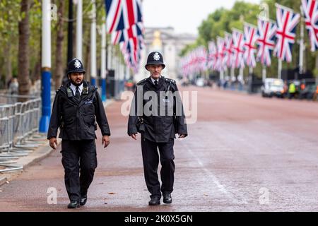 London, Großbritannien. 13. September 2022. Polizisten laufen an den Union Jack Flaggen vor dem Buckingham Palace auf der Mall Street vorbei. Die Menschen kommen weiterhin am Buckingham Palace an, da der Sarg mit dem Körper der längsten regierenden Monarchin, Königin Elizabeth II., voraussichtlich im Buckingham Palace eintreffen wird. Elizabeth II. Starb am 8. September in Schottland. Ihre Überreste nach den Zeremonien in Edinburgh werden am 13. September nach London verlegt und die Öffentlichkeit darf den Palast besuchen, um Respekt zu zollen. Kredit: SOPA Images Limited/Alamy Live Nachrichten Stockfoto