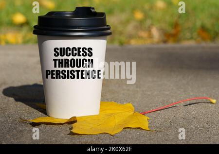 Auf dem gelben Ahornblatt gibt es eine Tasse Kaffee, auf dem - der Erfolg durch die Beharrlichkeit geschrieben ist. Geschäftskonzept. Stockfoto