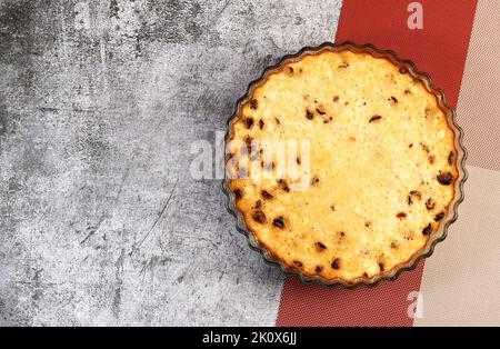 Quark-Auflauf mit getrockneten Preiselbeeren in einer Glasauflaufform auf dunkelgrauem Hintergrund. Draufsicht, flach liegend Stockfoto