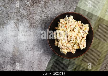 Hausgemachter russischer Salat oder Olivier aus gekochtem Gemüse und Wurst in einer Schüssel auf dunklem Hintergrund. Draufsicht, flach liegend Stockfoto