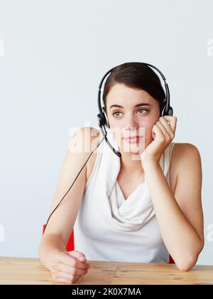 Fragen und Wünschen - Bestrebungen. Eine schöne junge Kundendienstvertreterin, die mit einem gelangweilten Gesichtsausdruck an einem Tisch sitzt. Stockfoto