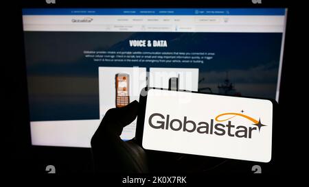 Person, die Mobiltelefon mit dem Logo des Satellitenkommunikationsunternehmens Globalstar Inc. Auf dem Bildschirm vor der Webseite hält. Konzentrieren Sie sich auf die Telefonanzeige. Stockfoto