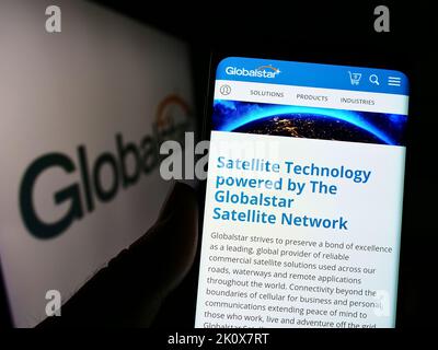 Person mit Mobiltelefon und Webseite des Satellitenkommunikationsunternehmens Globalstar Inc. Auf dem Bildschirm mit Logo. Konzentrieren Sie sich auf die Mitte des Telefondisplays. Stockfoto